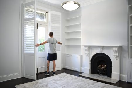 Shutters in a small room with a fireplace being installed by East Blinds